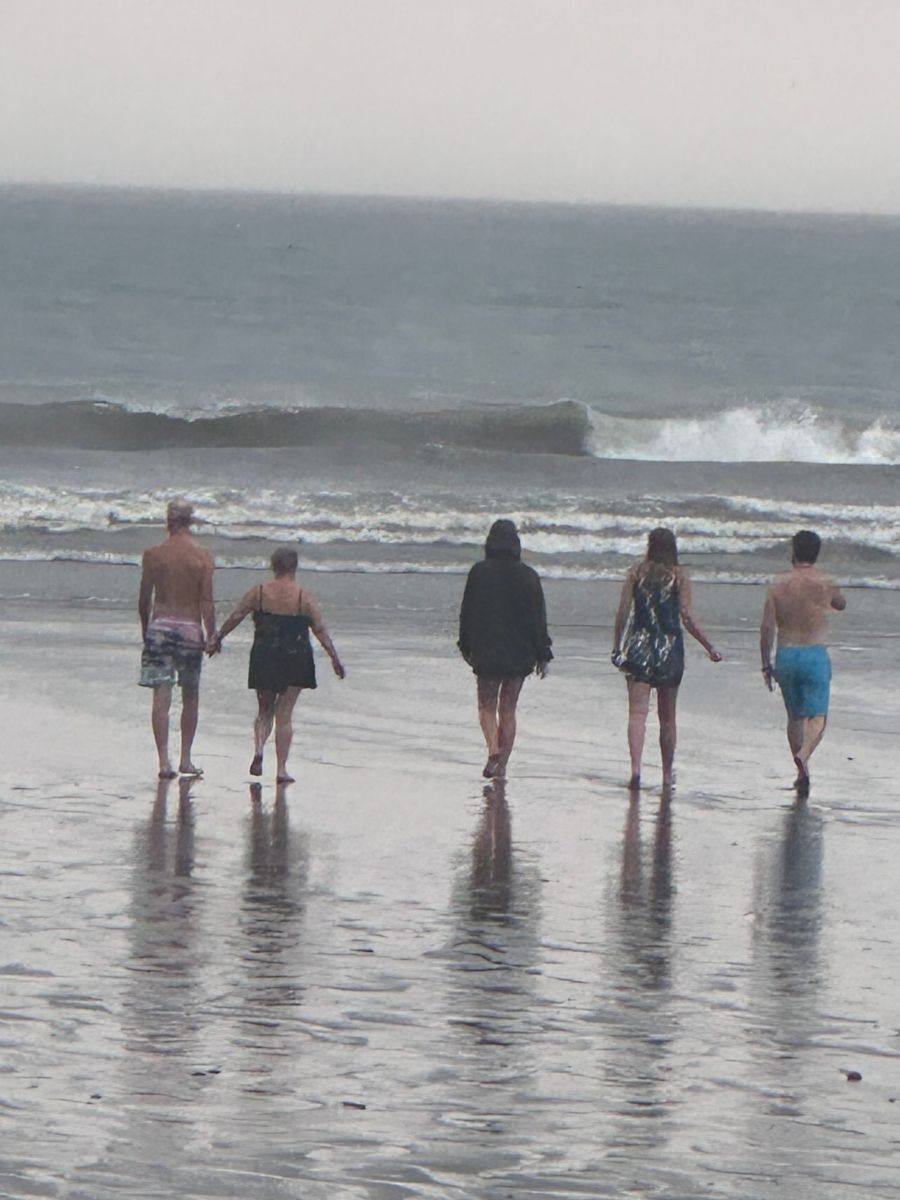 Five retreat guests walking side by side toward the surf on the beach in Jaco, Costa Rica